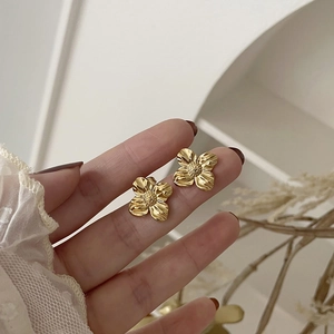 Detail showing gold irregular floral earrings held by hand for size reference