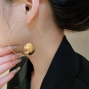 Detailed close-up of large golden geometric hoop earrings with hammered disk pendant