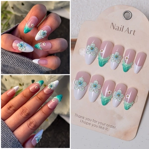 Detail of almond-shaped press-on nails with 3D blue flowers and gold microbeads