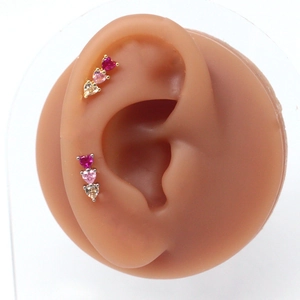 Macro view of triple heart stud earrings on model ear showing red and pink gradient gems