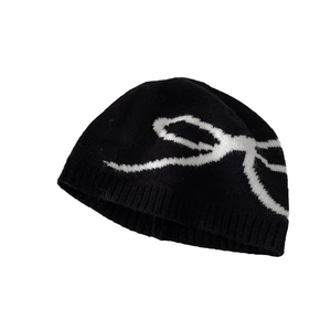 Women's black knit beanie featuring a white jacquard bow pattern on a plain background