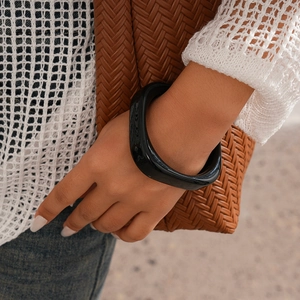 Macro detail of chunky black resin geometric bangle on wrist with knit sleeve