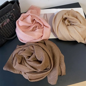Tre sciarpe plissettate luccicanti rosa, beige e marroni disposte a fiori su un tavolo