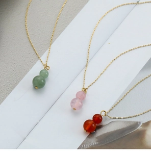 Close-up of colorful gourd pendants in green pink and red on fine gold necklace chains