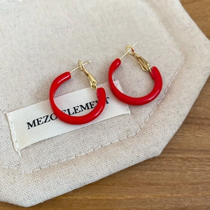 Detailed view of red resin hoop earrings with gold pins on a beige fabric pouch