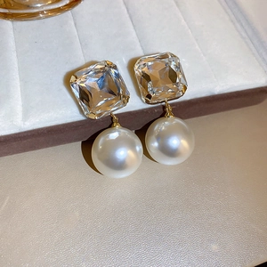 Detail of square crystal stud with white pearl drop on a soft jewelry display