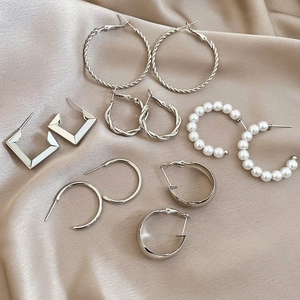 Detailed set of six pairs of silver-tone geometric earrings with pearls on silk fabric