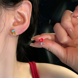 Detailed macro view of asymmetric colorful zircon stud earrings worn and held by model