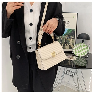 Model showcasing a cream pleated crossbody bag with a gold heart clasp and chain strap
