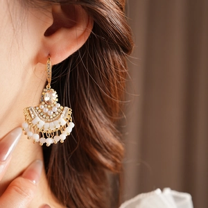 Détail de boucles d'oreilles dorées en éventail avec strass, perles et glands blancs