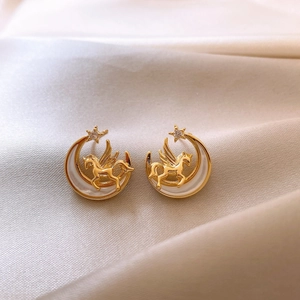 Close-up of golden unicorn and moon stud earrings with zircon on soft silk fabric