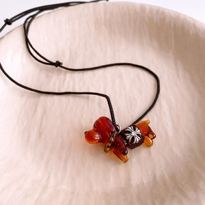 Détail d'un pendentif chiot en verre ambré sur cordon noir avec breloque fleurie argentée