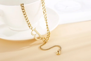 Dettaglio di una collana a catena cubana dorata con pendenti a B su una tazza bianca