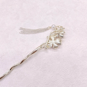 Détail d'une épingle à cheveux fleurie dorée avec perle blanche et pompons à chaînes fines