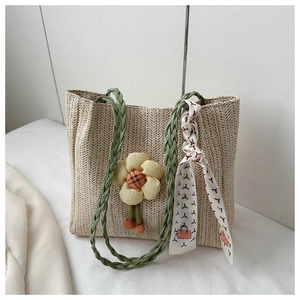 Detail of beige woven bucket bag with green handles, yellow flower, and decorative scarf