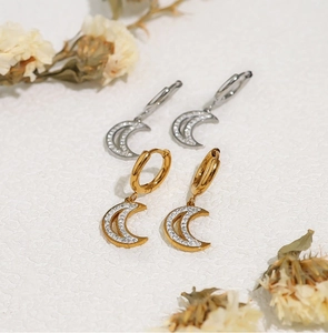 Close-up of gold and silver moon earrings inlaid with white zircon on a white surface