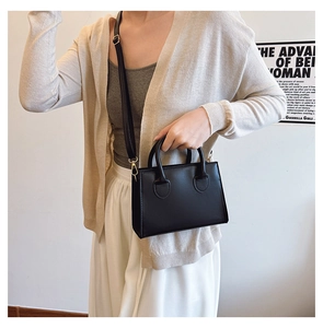 Detail of minimalist black handbag with dual handles and detachable shoulder strap on model