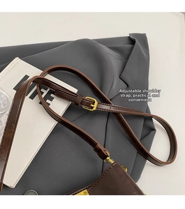 Detail of adjustable leather shoulder strap with gold buckle on a brown bucket bag