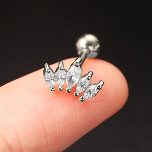 Macro view of a silver crown-shaped piercing stud with five marquise-cut zircons on a fingertip