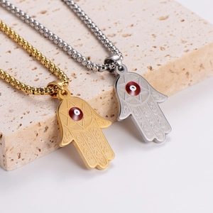 Gold and silver Hamsa hand necklaces with evil eye detail on stone display stand