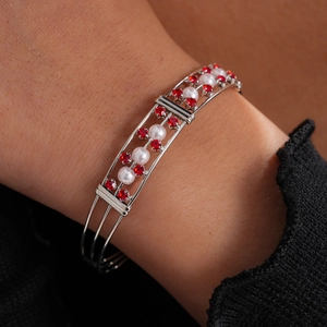 Nahaufnahme eines Silberarmbandes mit roten Strasssteinen und weißen Perlen am Handgelenk.