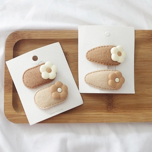 Detail view of milk tea colored floral hair clips for kids on a wooden display tray