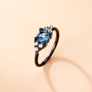 Macro detail of black plated ring featuring a blue gemstone center and zircon accents