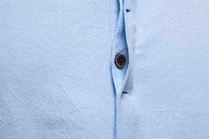Close-up of light blue cotton linen shirt showing premium fabric texture and brown button