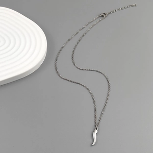 Detail of silver cornicello horn pendant on stainless steel chain over gray background