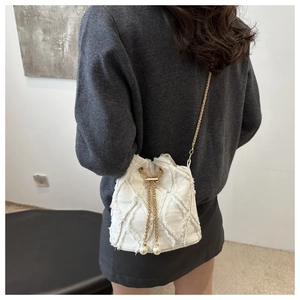 Detailed side view of a white denim bucket bag with gold chain and frayed floral texture