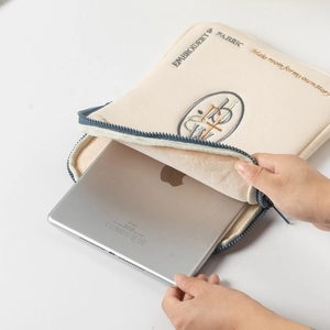 Detail showing hands sliding a silver iPad into the soft lined beige canvas sleeve