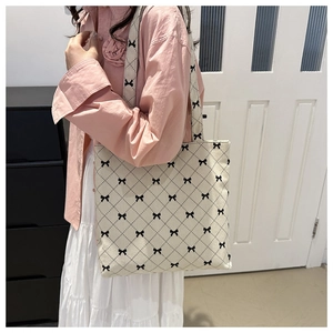 Close-up of beige tote bag with black bow pattern worn by a model in a bright interior