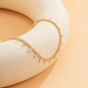 Detail of golden moon pendant chain accessory draped over a white geometric sculpture