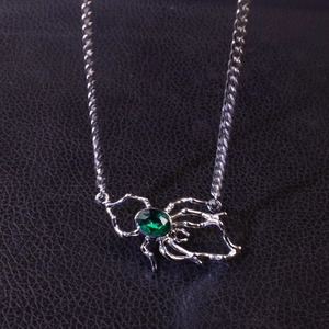 Silver spider pendant necklace with a green emerald gemstone on black leather background