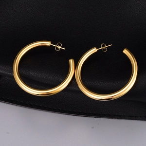Macro detail of large gold-plated hoop earrings with polished finish on black leather