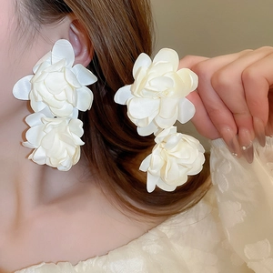 Détail de grandes boucles d'oreilles fleurs en satin blanc avec texture superposée