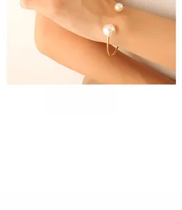 Detail view of adjustable open gold bracelet featuring dual pearls on a model's wrist