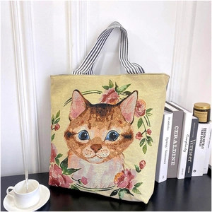 Detail of floral jacquard tote bag featuring embroidered ginger cat and striped handles