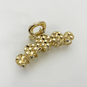 Detail of a golden metal hair claw clip featuring a unique woven texture and spring