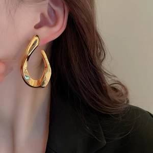 Macro shot of twisted oval gold metal earring showcasing smooth glossy texture on ear