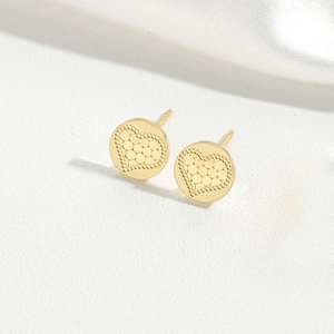 Macro shot of gold cross-textured heart earrings on white silk and leather backdrop