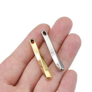 Pendentifs barres torsadées en or et argent tenus en main pour la création de bijoux