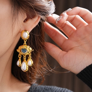 Close-up of vintage gold eye earrings with blue inlay and hanging pearl tassels