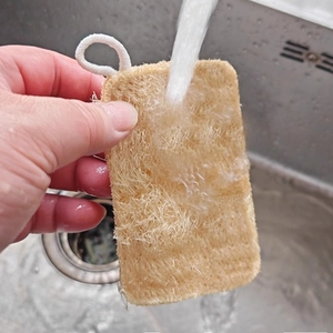 Natural loofah sponge for kitchen cleaning being rinsed under water in a stainless sink