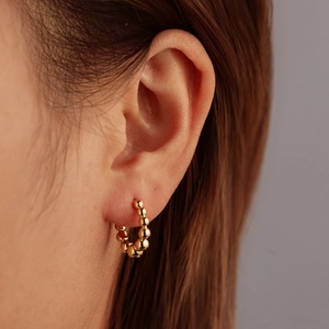 Polished gold beaded C-shaped stainless steel hoop earrings worn on female ear