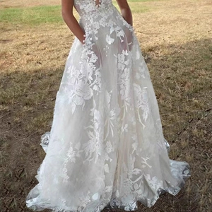 Elegant white lace A-line bridal gown with floral appliques on a garden lawn background