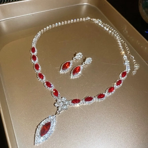 Detailed macro view of red crystal floral pendant and stud earrings set on gold tray
