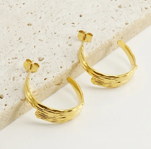 Macro detail of gold-plated geometric C-shape earrings on a textured stone base
