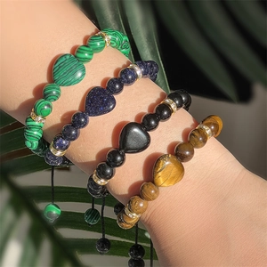 Close-up of stacked heart charm beaded bracelets in tiger eye and malachite stones
