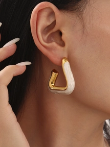 Close-up of golden triangular earrings with white marble inlay on female model ear